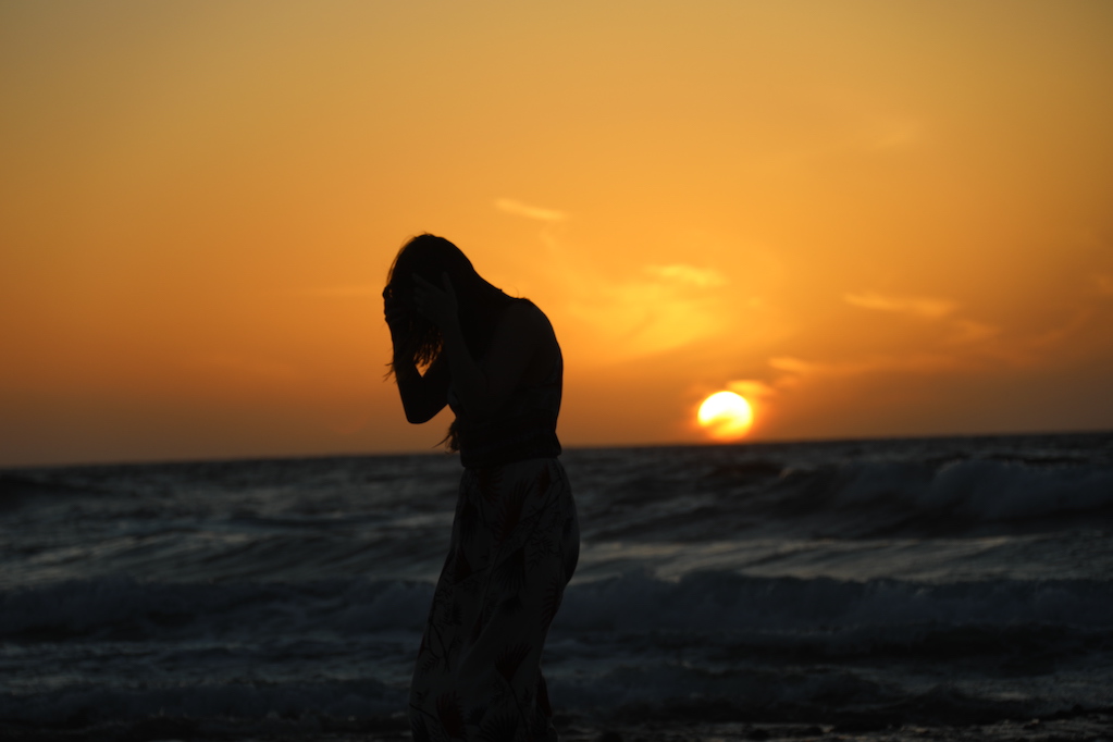 A silhouette of a woman at the ocean during the sunset